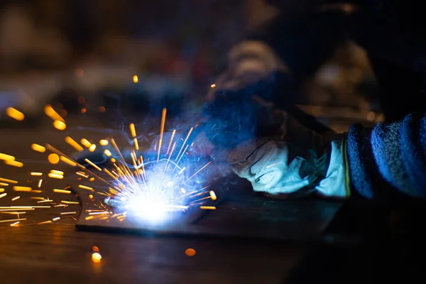 Metal welder works with a steel welder in a factory with protective equipment. Manufacture of metal structures and repair and construction services according to the concept of manual labor.