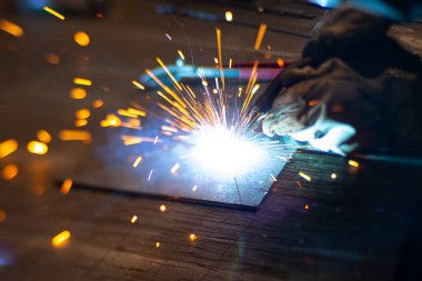 Metal kaynakçı, koruyucu ekipmanlı bir fabrikada çelik kaynakçıyla çalışıyor. Metal yapıların imalatı ve tamirat ve inşaat hizmetleri el işçiliği kavramına göre.