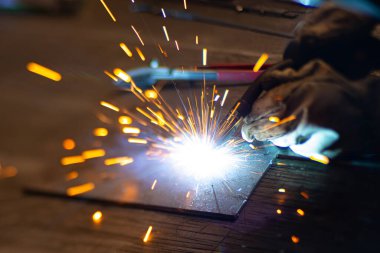 Metal kaynakçı, koruyucu ekipmanlı bir fabrikada çelik kaynakçıyla çalışıyor. Metal yapıların imalatı ve tamirat ve inşaat hizmetleri el işçiliği kavramına göre.