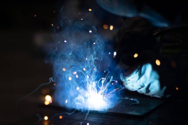 Metal kaynakçı, koruyucu ekipmanlı bir fabrikada çelik kaynakçıyla çalışıyor. Metal yapıların imalatı ve tamirat ve inşaat hizmetleri el işçiliği kavramına göre.