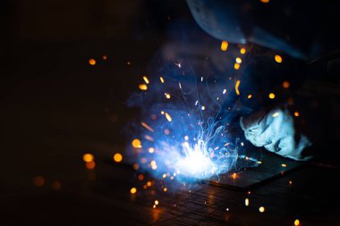 Metal kaynakçı, koruyucu ekipmanlı bir fabrikada çelik kaynakçıyla çalışıyor. Metal yapıların imalatı ve tamirat ve inşaat hizmetleri el işçiliği kavramına göre.