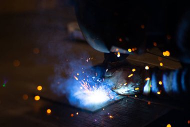 Metal kaynakçı, koruyucu ekipmanlı bir fabrikada çelik kaynakçıyla çalışıyor. Metal yapıların imalatı ve tamirat ve inşaat hizmetleri el işçiliği kavramına göre.