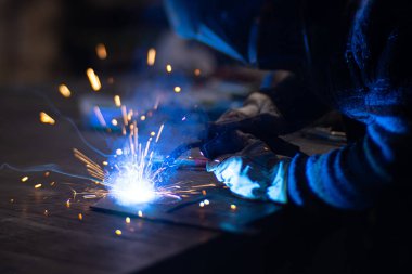 Metal kaynakçı, koruyucu ekipmanlı bir fabrikada çelik kaynakçıyla çalışıyor. Metal yapıların imalatı ve tamirat ve inşaat hizmetleri el işçiliği kavramına göre.