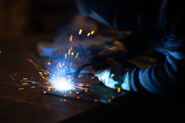 Metal kaynakçı, koruyucu ekipmanlı bir fabrikada çelik kaynakçıyla çalışıyor. Metal yapıların imalatı ve tamirat ve inşaat hizmetleri el işçiliği kavramına göre.