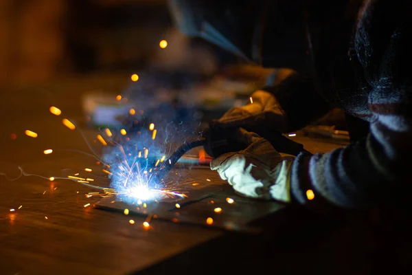 Metal welder works with a steel welder in a factory with protective equipment. Manufacture of metal structures and repair and construction services according to the concept of manual labor.