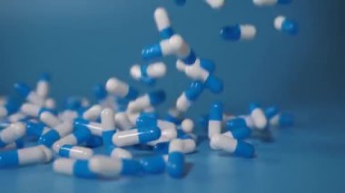 Blue medicine capsules fall on a blue background. Waterfall from medicinal capsules. Medical concept overdose. A group of antibiotic pill capsules falling