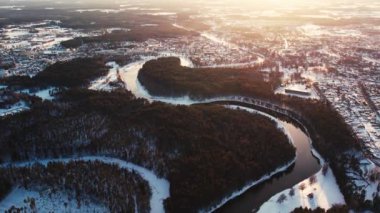 Küçük bir kasabanın yakınında, orman yığını olan dolambaçlı bir nehir. Kışın nehirde uçan bir dronun hava görüntüsü. Nehrin üzerinde gün batımı