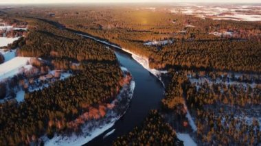 Küçük bir kasabanın yakınında, orman yığını olan dolambaçlı bir nehir. Kışın nehirde uçan bir dronun hava görüntüsü. Nehrin üzerinde gün batımı