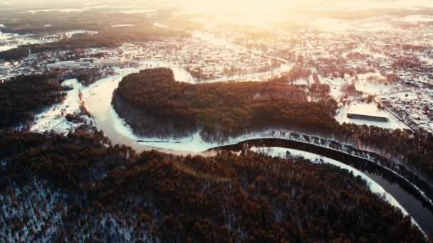 森の塊と小さな町の近くに巻き川 冬に川を飛ぶドローンの空中ビュー 川の上の夕日 — ストック動画