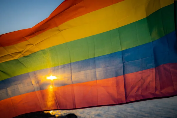 LGBT bayrağı gölün kenarında günbatımı arka planında. LGBT gay gurur bayrağı, lezbiyen, eşcinsel, biseksüel, transseksüel sosyal hareketler. Mutluluk özgürlük konsepti, eşcinsel çiftleri sevmek. Rüzgara karşı dalgalanan bir bayrak