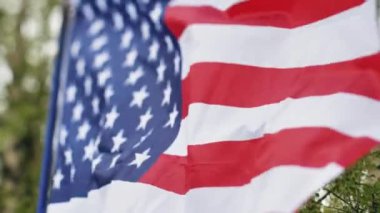 Amerikan bayrağı rüzgarda dalgalanıyor. Bayrak güzel yeşil ağaçların arka planında dalgalanıyor. Seçici yumuşak odak.