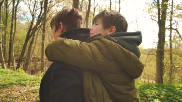 哥哥把小弟弟抱在怀里 弟弟坐在哥哥的背上 男孩们在森林里散步 软性选择性重点 — 图库视频影像