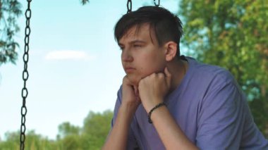 Adam depresif bir halde salıncakta oturuyor. Yalnızlık bunalımından muzdarip üzgün görünüşlü bir gencin yakın plan yüzü. Mutsuz savunmasız genç adam stresin üstesinden geliyor.