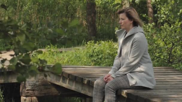 一个女人正坐在一座抑郁的木头桥上 忧心忡忡的忧郁症女子的近视脸 处理压力的脆弱的年轻妇女很不快乐 — 图库视频影像