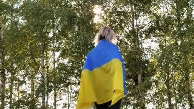 Sırtında Ukrayna bayrağı olan bir kadın. Bayrağı olan bir Anma Günü. Ukrayna bayrağı taşıyan üzgün kadın