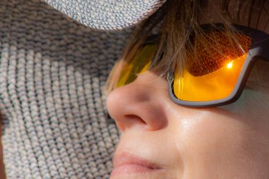 Şapkalı ve güneş gözlüklü bir kadın sahilde güneşleniyordu. Yumuşak odaklı portre. Sıcak yaz, güneş ve kadın