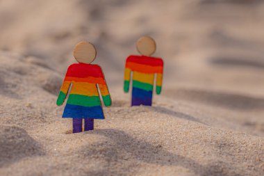 Kumsaldaki LGBT ahşap insanlar. Plajda duran çift, gökkuşağı bayrağıyla, eşit haklar, LGBT topluluğunun sembolü. Kumlu bir sahilde LGBT bayrağı. Yaz yolculuğu konsepti. Aynı cinsiyetin sembolü.
