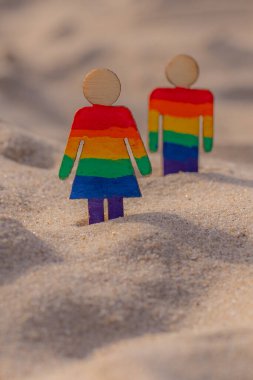 Kumsaldaki LGBT ahşap insanlar. Plajda duran çift, gökkuşağı bayrağıyla, eşit haklar, LGBT topluluğunun sembolü. Kumlu bir sahilde LGBT bayrağı. Yaz yolculuğu konsepti. Aynı cinsiyetin sembolü.