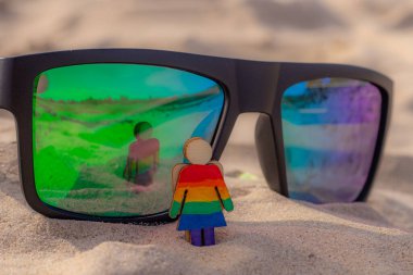Kumsaldaki LGBT ahşap insanlar. Plajda duran çift, gökkuşağı bayrağıyla, eşit haklar, LGBT topluluğunun sembolü. Kumsalda LGBT bayrağı olan güneş gözlükleri. Yaz yolculuğu konsepti.