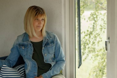 Pencerenin yanında nazik, tatlı bir kadın oturuyor. Hayat sahnesinde kadın yalnızlığı. Karakterli bir kadın pencere kenarında poz verir.