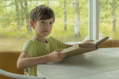 Bir çocuk masaya oturur ve eski bir kitap okur. Elinde kitap olan bir çocuk. Kitaplı bir çocuk dersi.