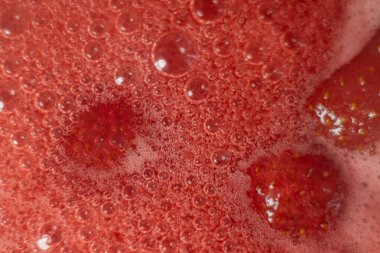 Çilek reçeli için pembe köpük. Çilekler şekerli bir tencerede kaynatılır. En lezzetli ev yapımı çilek reçeli. Köpük üzerine yumuşak seçici odaklanma. Kısmen şekilli soyut bir resim.