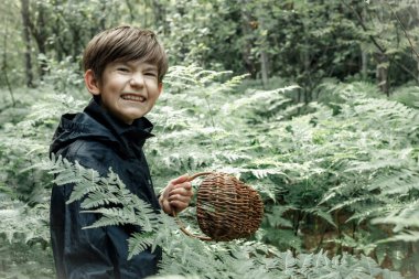 Ağzında hasır sepeti olan bir çocuk. Bir çocuk ormanda tek başına mantar topluyor. Yumuşak seçici odak