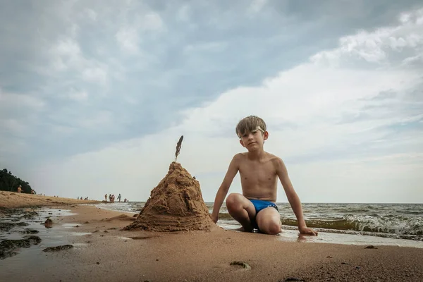 Bir çocuk deniz kıyısında kumdan bir piramit yaptı. Bir çocuk denizin kumlu sahilinde deniz kumlarıyla oynuyordu. Yumuşak seçici odak