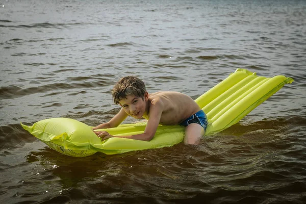 A boy on an inflatable mattress in the sea. A smiling child is swimming in the sea with an inflatable mattress. Soft selective focus