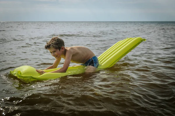 一个躺在海里充气床垫上的男孩一个笑着的孩子带着一个充气床垫在海里游泳 软性选择性重点 — 图库照片