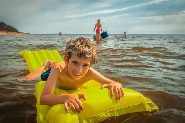A boy on an inflatable mattress in the sea. A smiling child is swimming in the sea with an inflatable mattress. Soft selective focus