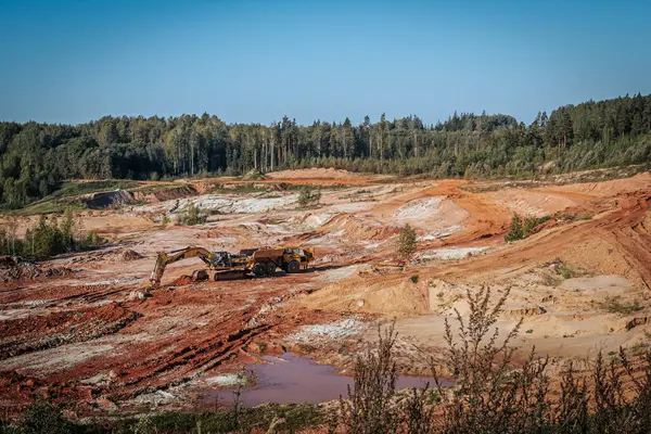 stock image A heavy machine with a trailer works in a sand quarry. The excavator loads sand and clay into the machine.