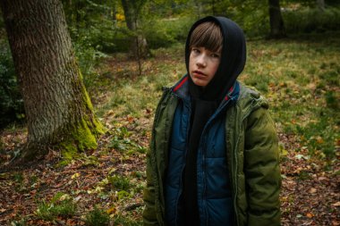 Sonbahar ormanında bir çocuk. Başında başlığı olan bir çocuk.