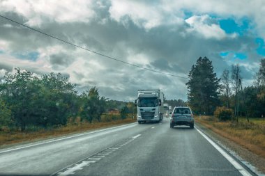 Riga karayolu trafiği asfaltlanmış. Letonya yollarında trafik. Asfalt kaplamalı yol. Ağır ve hafif araç hareketi. Yaklaşan fırtınada ağır bulutlar.