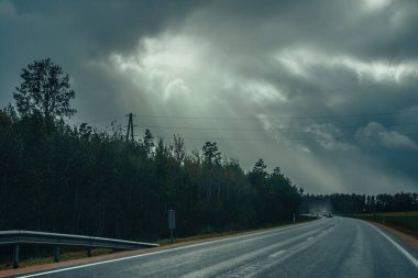 Riga karayolu trafiği asfaltlanmış. Letonya yollarında trafik. Asfalt kaplamalı yol. Ağır ve hafif araç hareketi. Yaklaşan fırtınada ağır bulutlar.