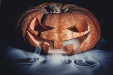 Cadılar Bayramı balkabağı duman içinde. Cadılar Bayramı balkabağı gülüşü ve parti için korkunç gözler. Siyah arka planda parlayan gözleri olan korkunç bir Cadılar Bayramı balkabağı görüntüsü. Seçici Yumuşak Odaklanma