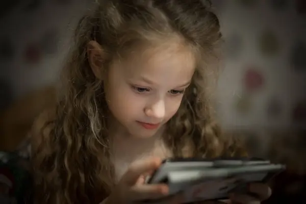 Child Concentration, Female Digital Native Looking Down Holding Technology. A concentrated female digital native looking down while holding technology. Soft selective focus