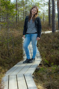 Bataklık yolunda yürüyen ve kameraya poz veren kadın.