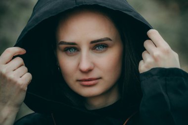 Siyah kapüşonlu bir kadın, yüzü gizlilik için bulanık, dışarıda duruyor.