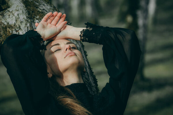 A woman in a linden alley in a dark checkered coat with long hair on a blurred natural background