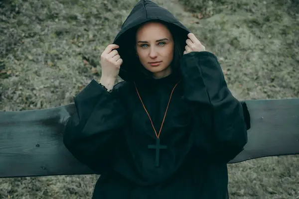 A woman in a black hoodie, hood up, face blurred for privacy, stands outdoors