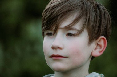 Oğlan tahta bir bankta oturur ve kameraya poz verir.