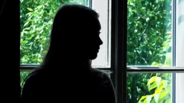 Pencerenin kenarında duran bir kadının siyah silueti yalnızlık ve depresyon hissi uyandırıyor. Karanlık figür ve dışarıdaki ışık arasındaki zıtlık duygusal derinliği vurgular.