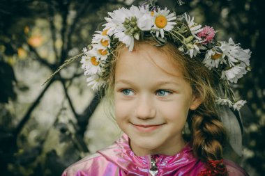 Mavi gözlü ve nazik bir gülümsemesi olan genç bir kız papatya tacı ve yonca çiçeği takıyor. Dışarıda bir bahçede pembe bir ceket giyerek dikiliyor. Arkaplanda bulanık yeşil yeşillik.
