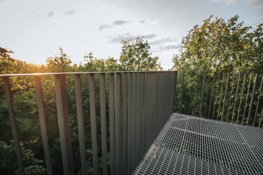 Letonya 'daki Zilakalnas gözetleme kulesinin, açık bir gökyüzünün altında yemyeşil ağaçlarla çevrili çarpıcı manzarası. Kulenin çelik yapısı belirgin bir şekilde...