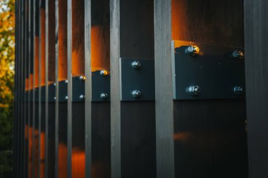 Ilık güneş ışığı bir yapının metal iskeletinde parıldar, kirişlerin üzerine altın renkler ve gölgeler bırakır. Yeşilliğin yemyeşil manzarası boşluklardan görülebilir. Boşluğu kopyala.