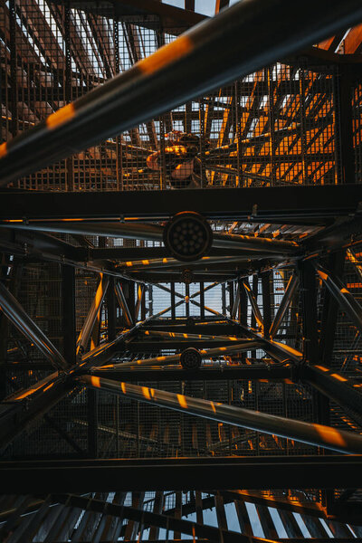 Теплый солнечный свет проникает сквозь металлическую структуру здания, отбрасывая на лучи золотые оттенки и тени. Вид на пышный зеленый пейзаж можно увидеть через пробелы. Свободное место для копирования.