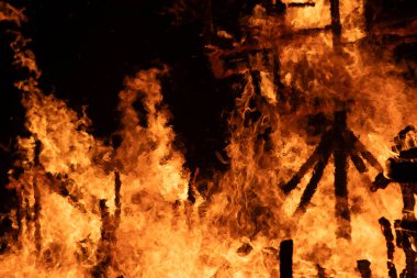 Ahşap kütükleri yutan yoğun bir ateşin yakın plan görüntüsü. Parlak alevler ve parlayan közler dramatik ve güçlü bir görüntü yaratır, ateşin ham enerjisini ve yıkıcı gücünü yakalar..
