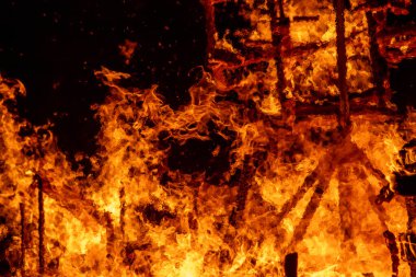 Ahşap kütükleri yutan yoğun bir ateşin yakın plan görüntüsü. Parlak alevler ve parlayan közler dramatik ve güçlü bir görüntü yaratır, ateşin ham enerjisini ve yıkıcı gücünü yakalar..