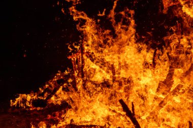 Ahşap kütükleri yutan yoğun bir ateşin yakın plan görüntüsü. Parlak alevler ve parlayan közler dramatik ve güçlü bir görüntü yaratır, ateşin ham enerjisini ve yıkıcı gücünü yakalar..